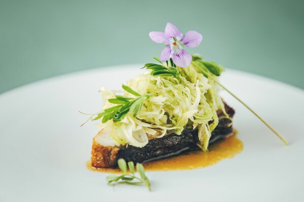 A dish with a flower garnish on a white plate. - Auberge eaufeu (Komatsu)