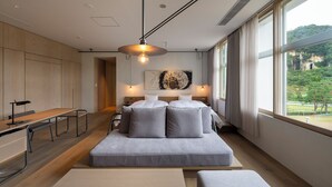 A modern bedroom with a large bed, bedside tables, a desk, and a view of greenery. - Auberge eaufeu (Komatsu)