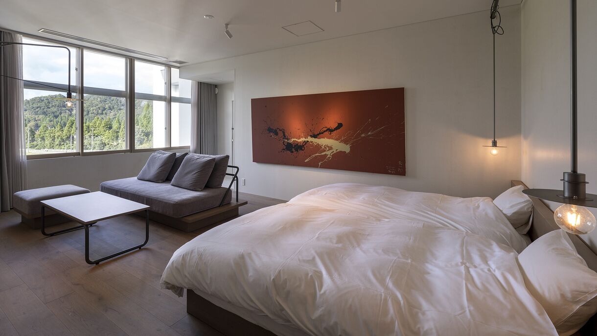 Een moderne slaapkamer met een groot bed, een bank, een klein tafeltje en een schilderij aan de muur.