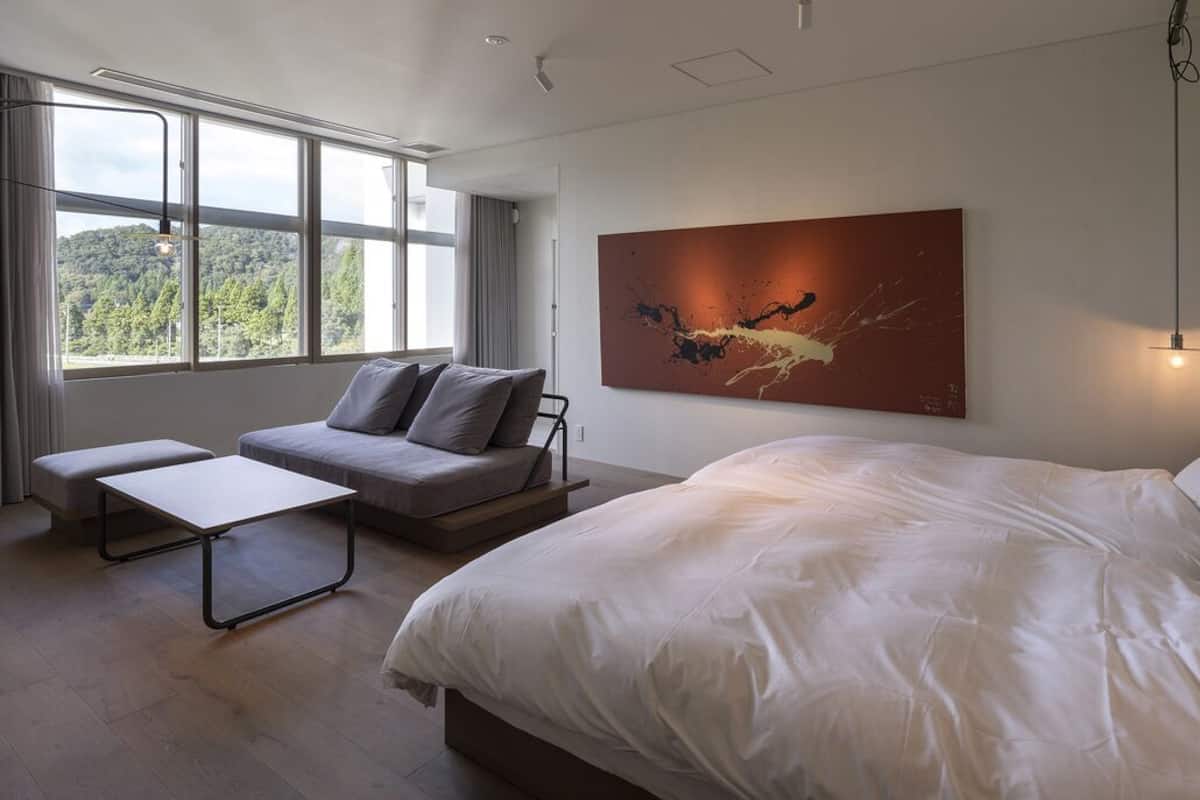 Een moderne slaapkamer met een groot bed, een bank, een klein tafeltje en een schilderij aan de muur.