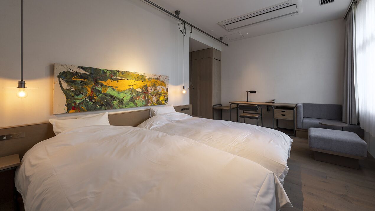 Een hotelkamer met een groot bed, een bureau, een stoel en een kleurrijk abstract schilderij aan de muur.