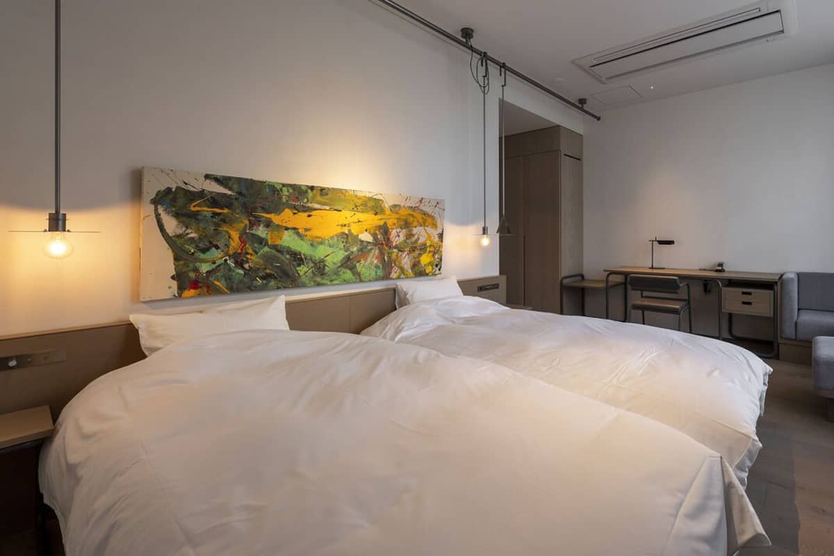 Een hotelkamer met een groot bed, een bureau, een stoel en een kleurrijk abstract schilderij aan de muur.