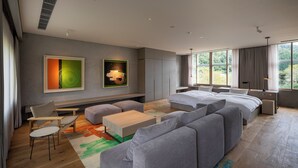A modern hotel room with a large bed, a sofa, a small table, and a chair. There are two paintings on the wall and a large window with a view of trees. - Auberge eaufeu (Komatsu)