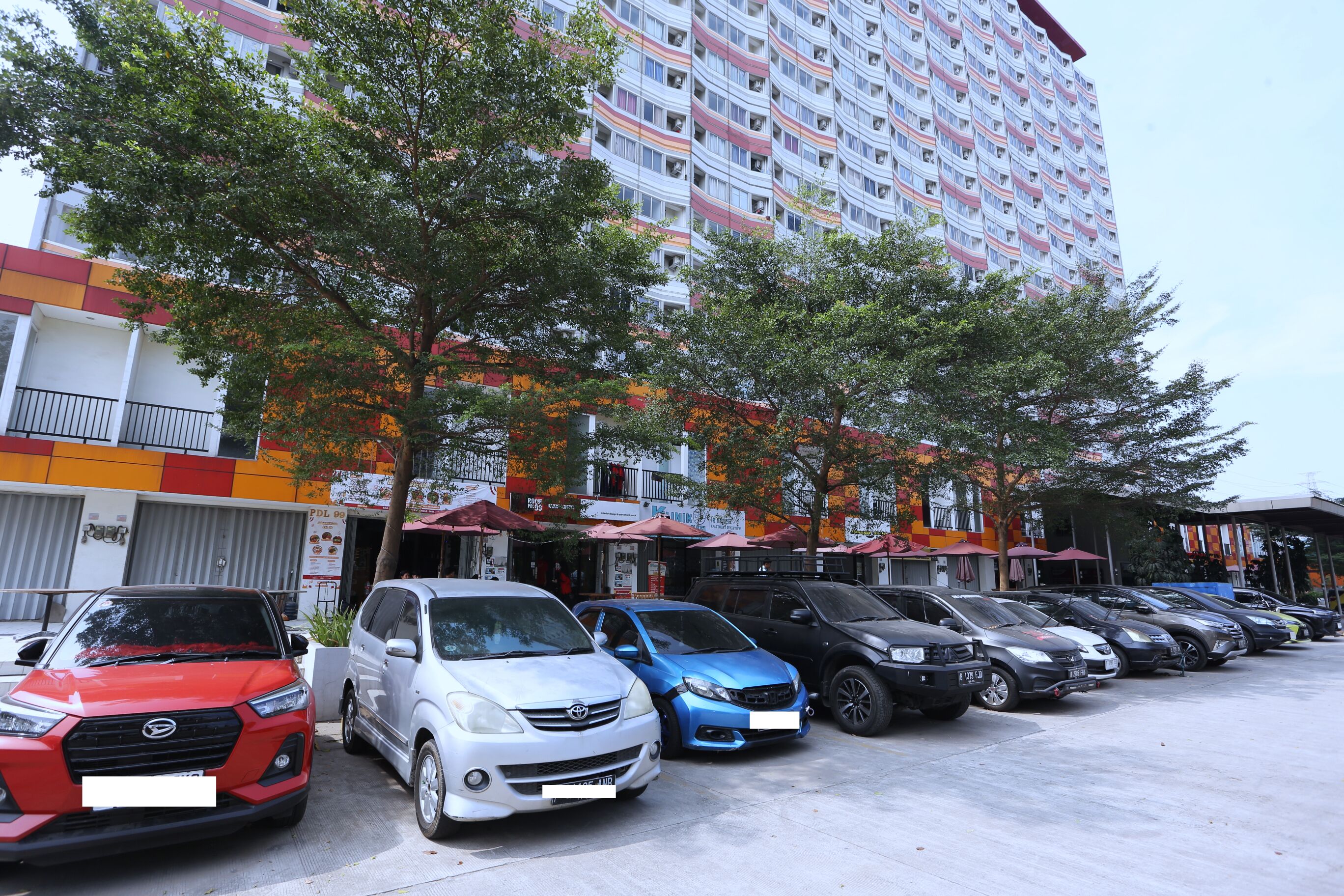 A parking lot with multiple cars parked in front of a multi-story building with balconies.