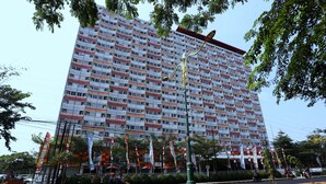 A multi-story building with a uniform facade, a street in front with a few pedestrians, and some greenery. - Nusantara Rooms Mahakam By Reccoma (Cikarang)