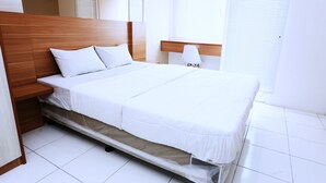 A neatly made bed with white bedding, a wooden headboard, and a bedside table with a lamp. - Nusantara Rooms Mahakam By Reccoma (Cikarang)