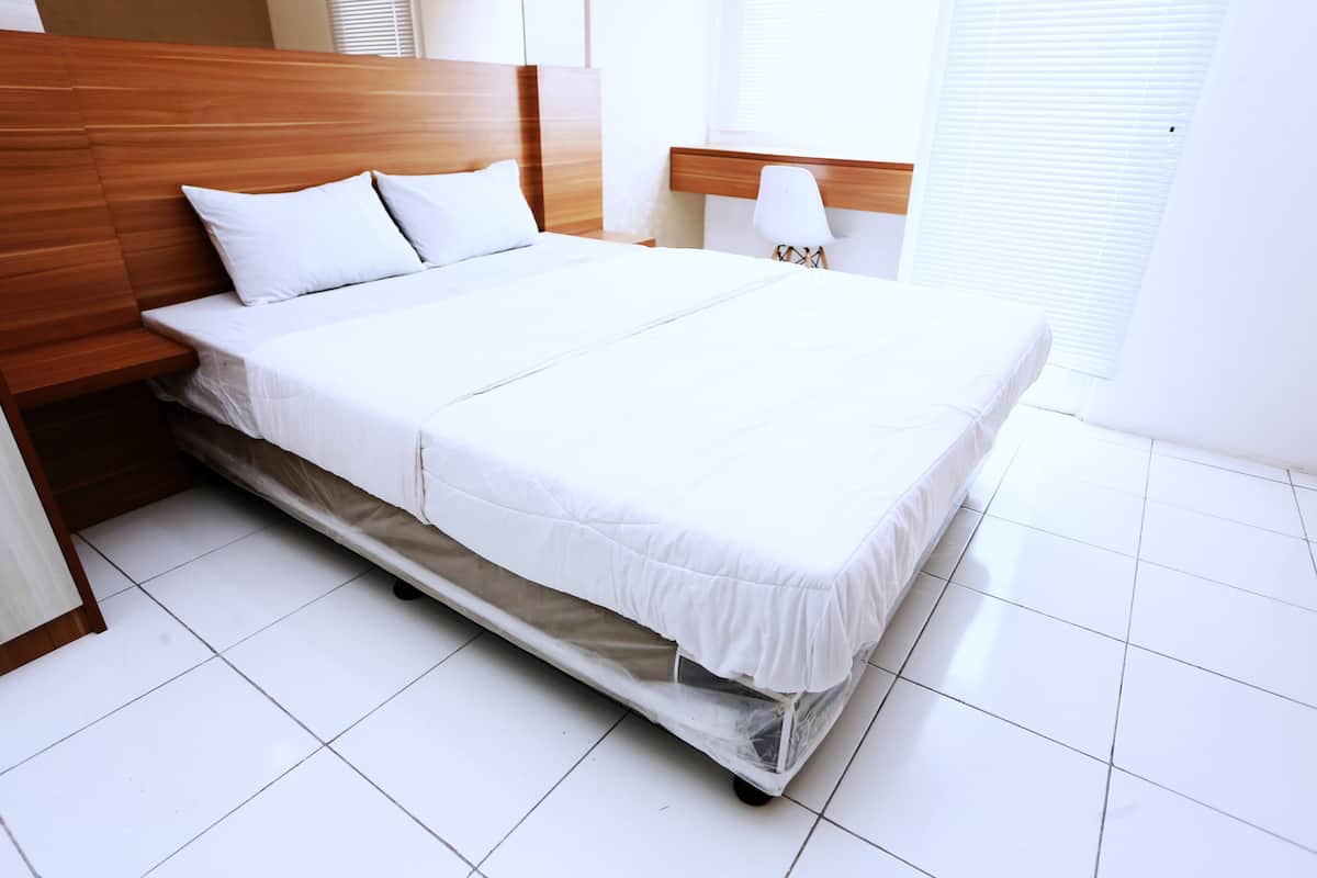 Una cama bien hecha en una habitación de hotel, con cabecera de madera, ropa de cama blanca y suelo blanco.