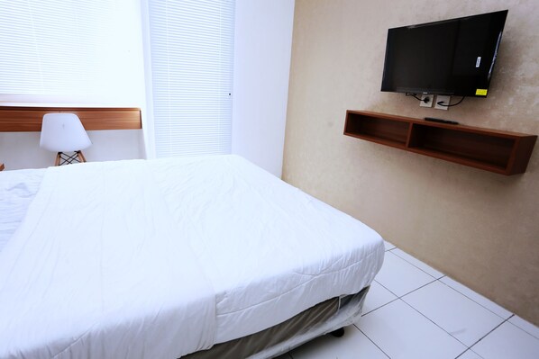 Une chambre d’hôtel avec un grand lit, un téléviseur fixé au mur et une table de chevet avec une lampe.