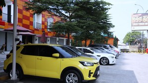 A row of parked cars in a parking lot with a building featuring a checkered facade in the background. - Nusantara Rooms Mahakam By Reccoma (Cikarang)