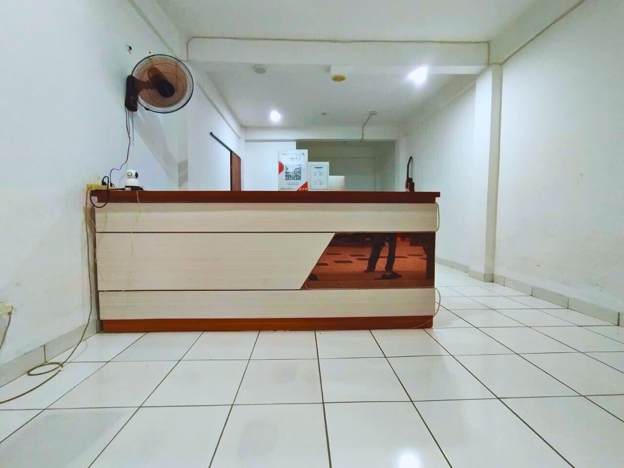 A reception area with a counter, a wall-mounted fan, and a tiled floor.