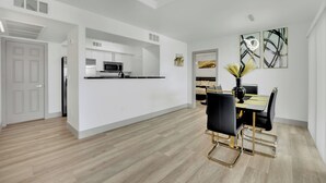 A modern kitchen with white cabinetry, a central island, and a dining area with a black and gold table and chairs. - Charming 2-bedroom condo near to Strip (Las Vegas)