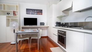 A modern kitchen with white cabinetry, a dining area with a table and chairs, a flat-screen TV, a microwave, and a stove. - GuestHost - Cozy 38 sqm apartment for 2 people, located near the Porta di Aquileia in Udine. It features a reserved covered parking space for guests, offering comfort and convenience. The area is rich in history and charm, just steps away from Udine's hi (Udine)