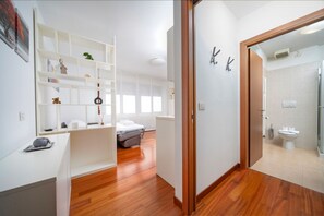 Ein modernes Hotelzimmer mit Holzboden, einem Bett, einem weißen Kleiderschrank und einem Badezimmer mit Toilette und Dusche.