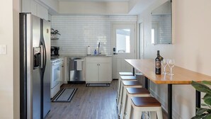 Une cuisine moderne avec des meubles blancs, un réfrigérateur en acier inoxydable, un comptoir-bar en bois et des tabourets.