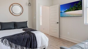 Une chambre à coucher avec un lit, un miroir rond, une lampe suspendue, une porte et un tableau représentant une vue sur la plage.