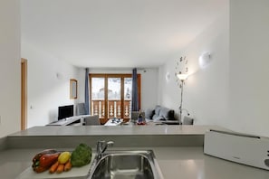 A modern kitchen with a sink, a cutting board with vegetables, a dining area with a table and chairs, and a view of a snowy landscape through the window. - Family-Friendly Andorra Accommodation (El Tarter)