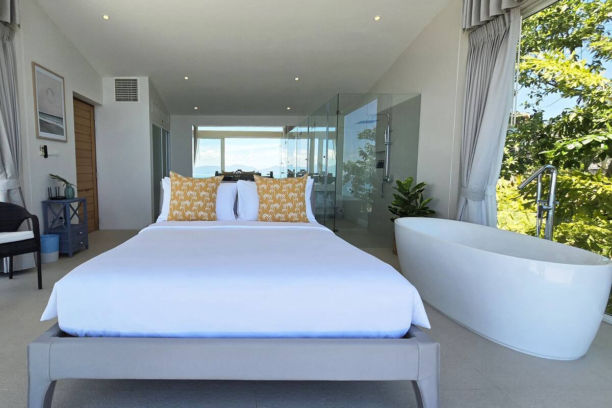 A modern bedroom with a large bed, a glass-enclosed shower, and a view of the outdoors.
