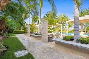 Un área de piscina en un complejo turístico con sillones de descanso, palmeras y cielo despejado.