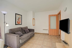 A living room with a sofa, a television, a framed picture, a lamp, and a door. - Andorra Friends' Ski Apartment (El Tarter)