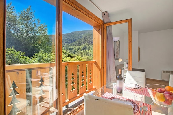 A balcony with a clear view of a forested hillside, a dining table with a glass top, and a chair. - Andorra Friends' Ski Apartment (El Tarter)