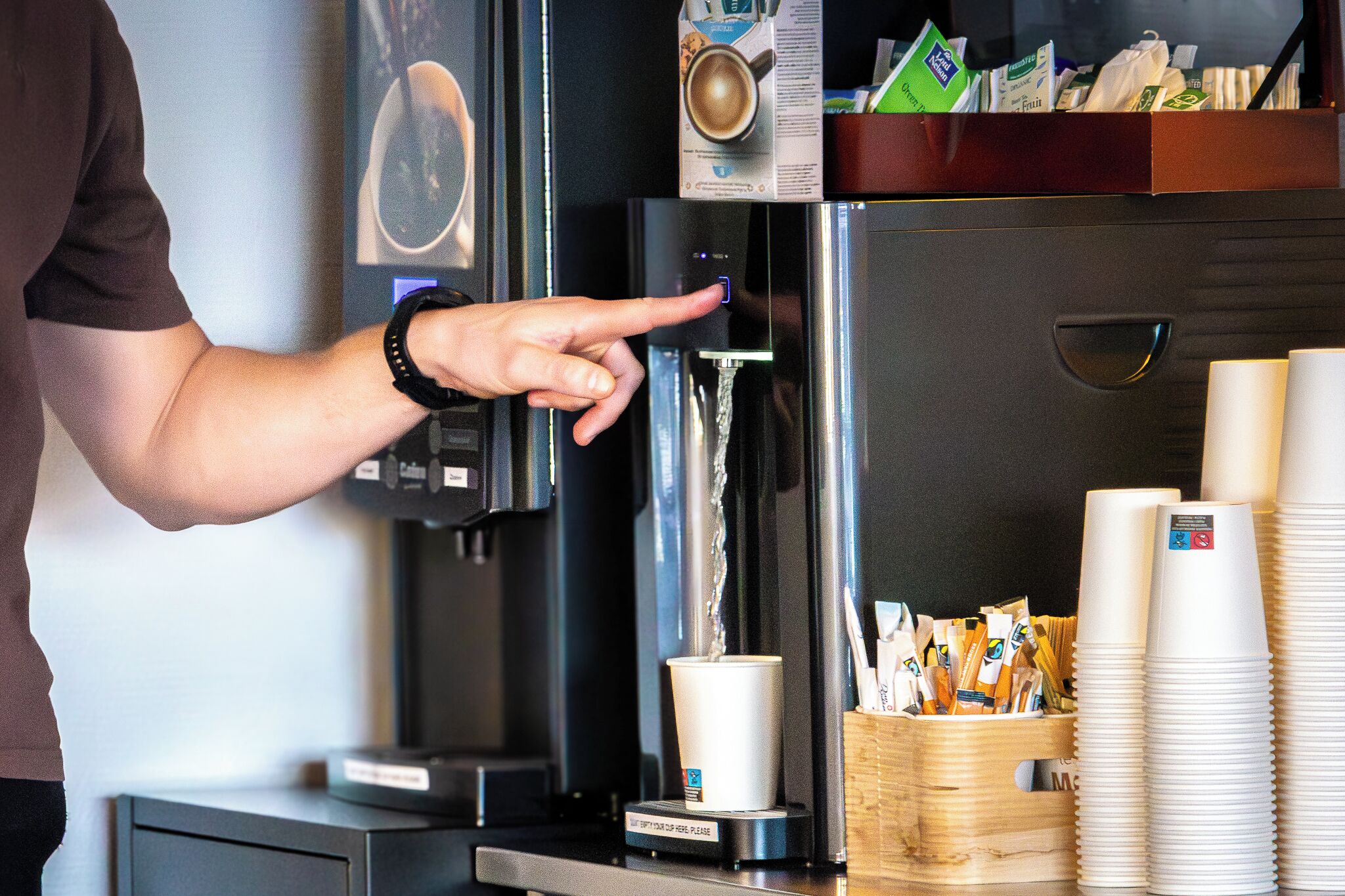 A coffee machine with a cup dispenser, a coffee cup, and a stack of disposable cups.