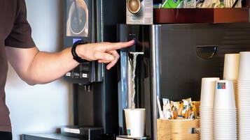 A coffee machine with a cup dispenser, a coffee cup, and a stack of disposable cups.