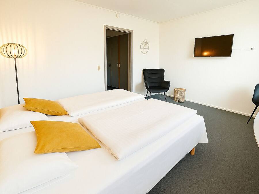 Habitación de hotel con dos camas, una silla, un televisor y una lámpara.