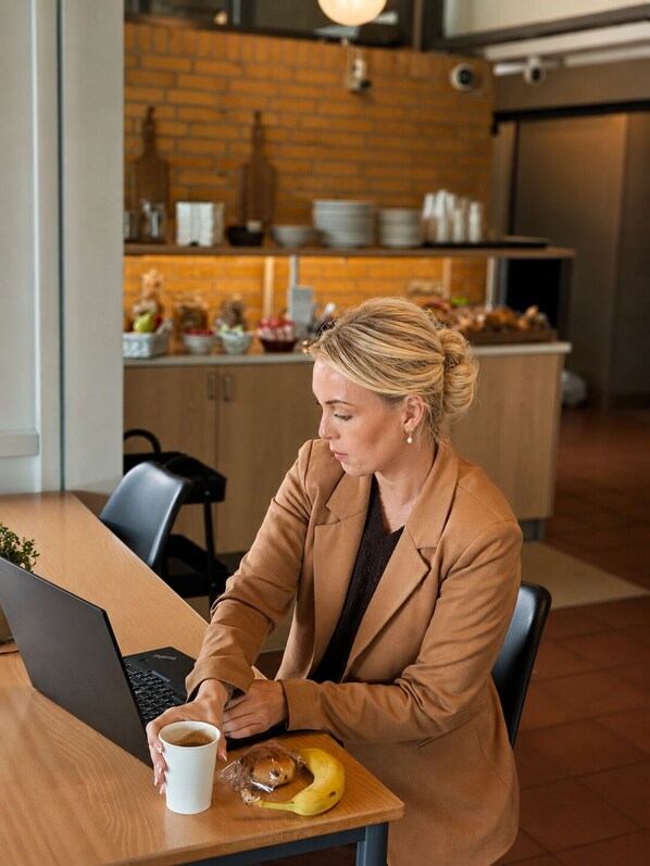A person seated at a table with a laptop, a cup, and a banana. - Hotel Svanegården (Korsor)