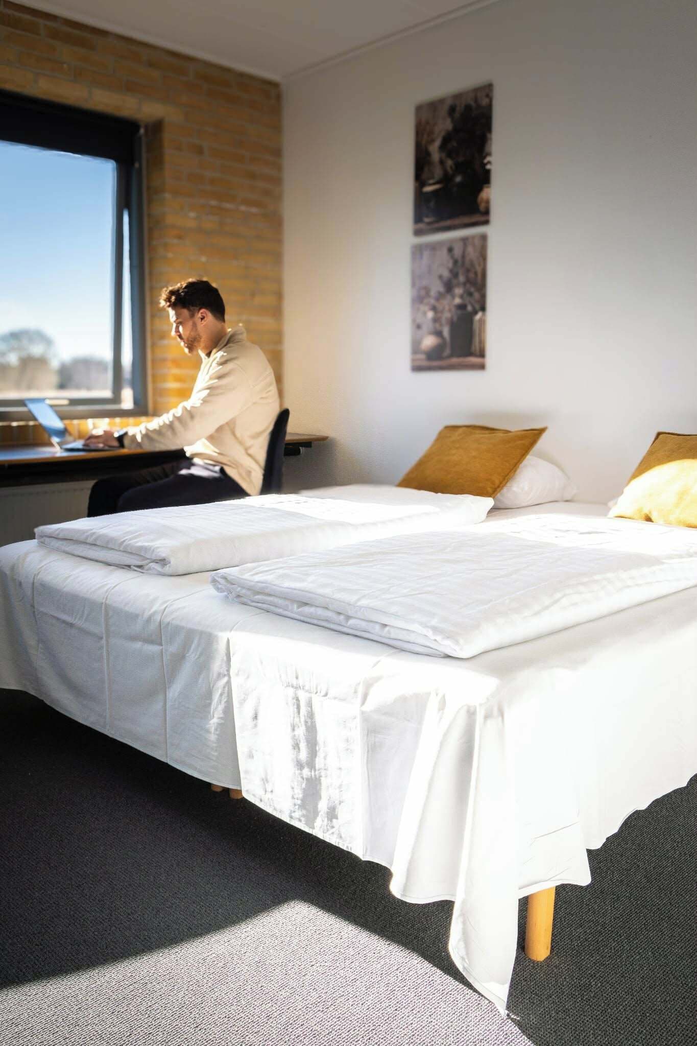 Habitación de hotel con una cama grande, un escritorio con una computadora portátil y una ventana con vistas al exterior.