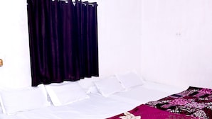 A bedroom with a bed, white bedding, a purple floral bedspread, a ceiling fan, and an air conditioning unit. - SHIVAY GUEST HOUSE (Deoghar)