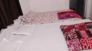 A bed with floral and leopard print bedding, a white pillow, and a dark curtain. - SHIVAY GUEST HOUSE (Deoghar)