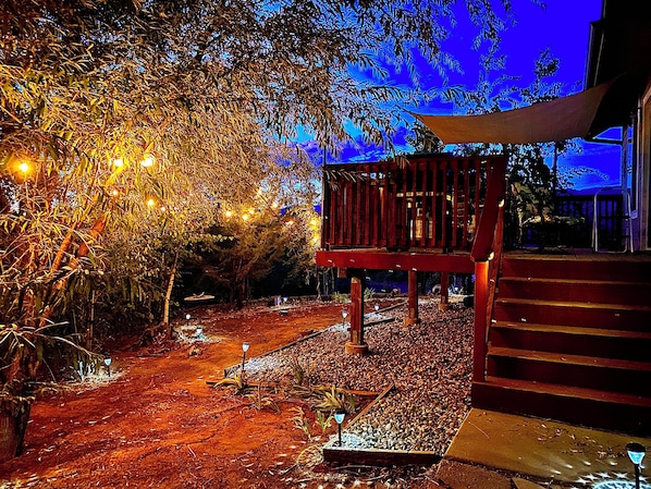 A wooden deck with a railing, surrounded by trees and a pathway.