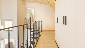 Una escalera con piso de madera y techo de piedra, que conduce a una habitación con paredes blancas y una puerta.