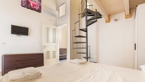 Un dormitorio con una cama, un televisor montado en la pared, un cabecero de madera, una escalera de caracol y una puerta que da a otra habitación.