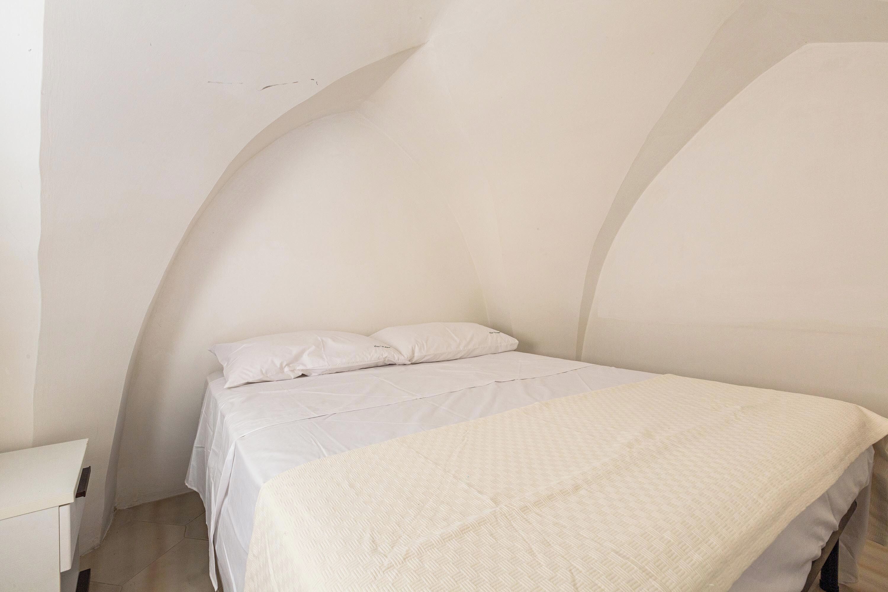 A bedroom with a bed, white bedding, and a nightstand.