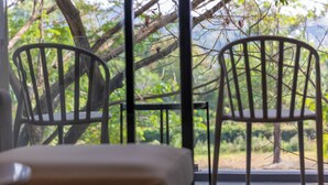 A room with two metal chairs and a small table, a window with a view of greenery outside. - City Gate Kamala 5 Rated  P209 c33 (Kamala)