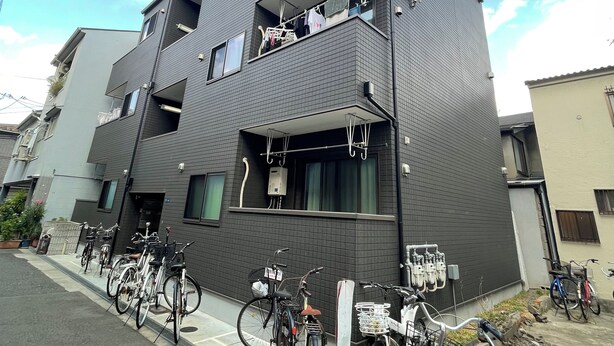 Un immeuble résidentiel moderne à plusieurs étages, doté de balcons, avec des vélos garés à l’extérieur et un ciel dégagé.