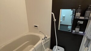 Une salle de bain moderne avec une baignoire, une douchette à main et un petit lavabo.