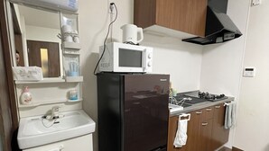 Une cuisine compacte avec un réfrigérateur noir, un four à micro-ondes, un évier, des armoires en bois et une cuisinière.