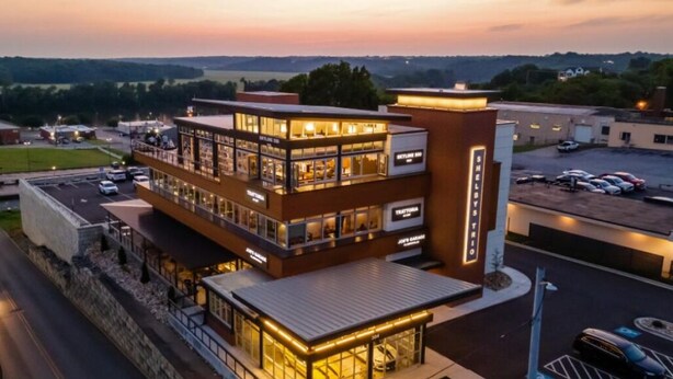 A multi-story hotel with a glass facade, a separate entrance building, and a parking lot.