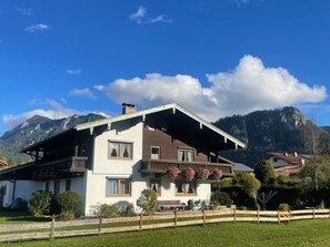 Un chalet à deux étages doté d’un balcon, entouré d’une clôture en bois, et situé dans un cadre montagneux.