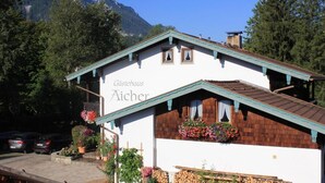 Et traditionelt alpebondehus med en træfacade, kaldet "Gästehaus Aicher", omgivet af frodig vegetation og bjerge.