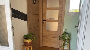 Eine Holztür mit einem 'privado'-Schild, ein Blumentopf auf einem Hocker und eine gewebte Matte am Boden.
