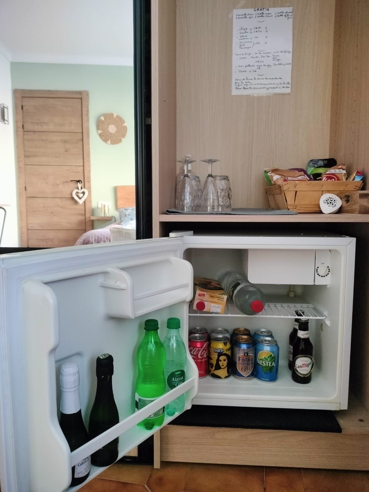 A refrigerator with beverages and snacks, a wooden door, and a wall with a menu.