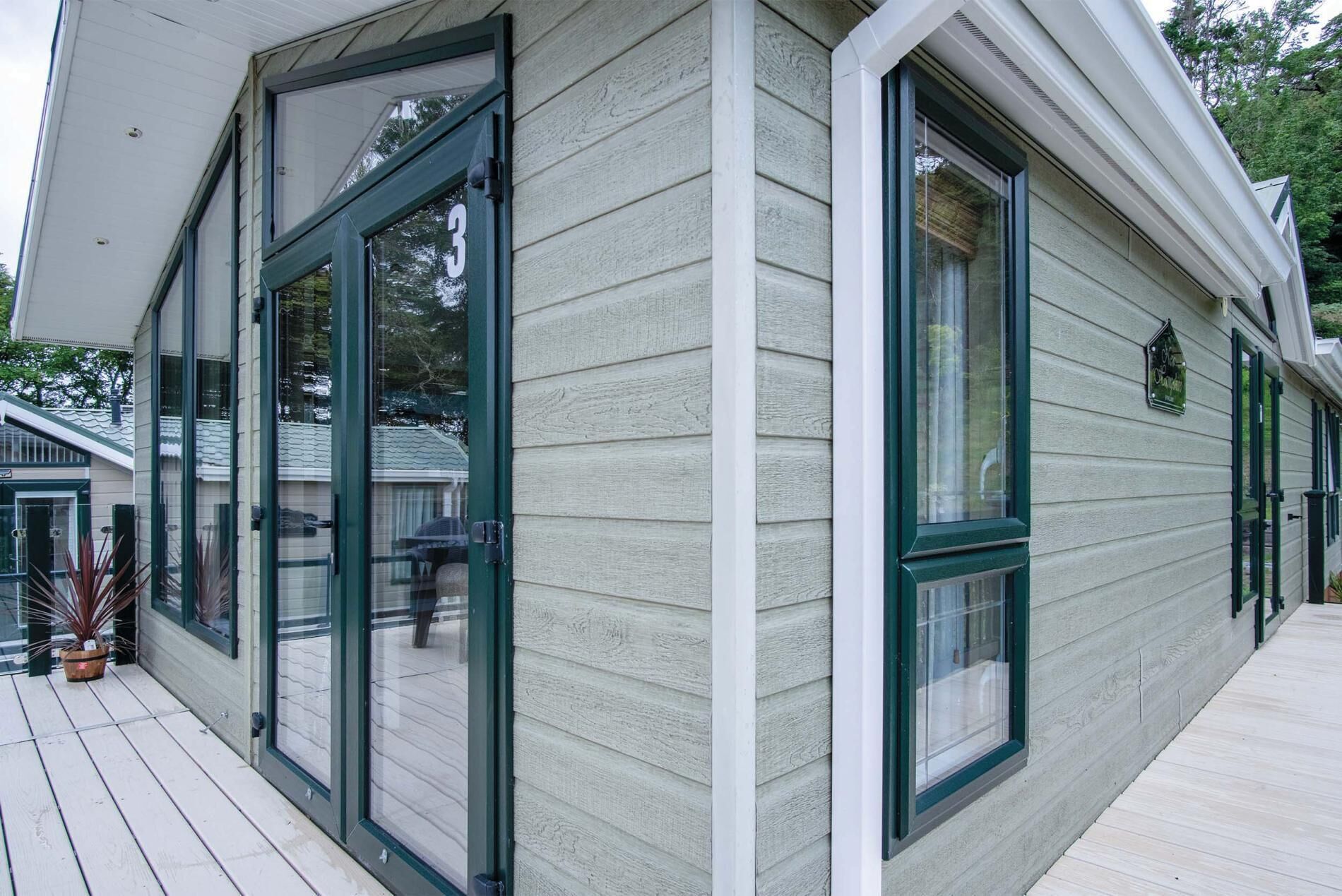 A corner of a house with large glass doors and windows, a wooden deck, and a small sign on the wall.