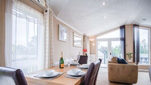 A dining area with a wooden table set for four, a bottle of champagne, and a vase of red flowers. - 3 Manor Lodge - 2 Bedroom Lodge - Pendine (Carmarthen)