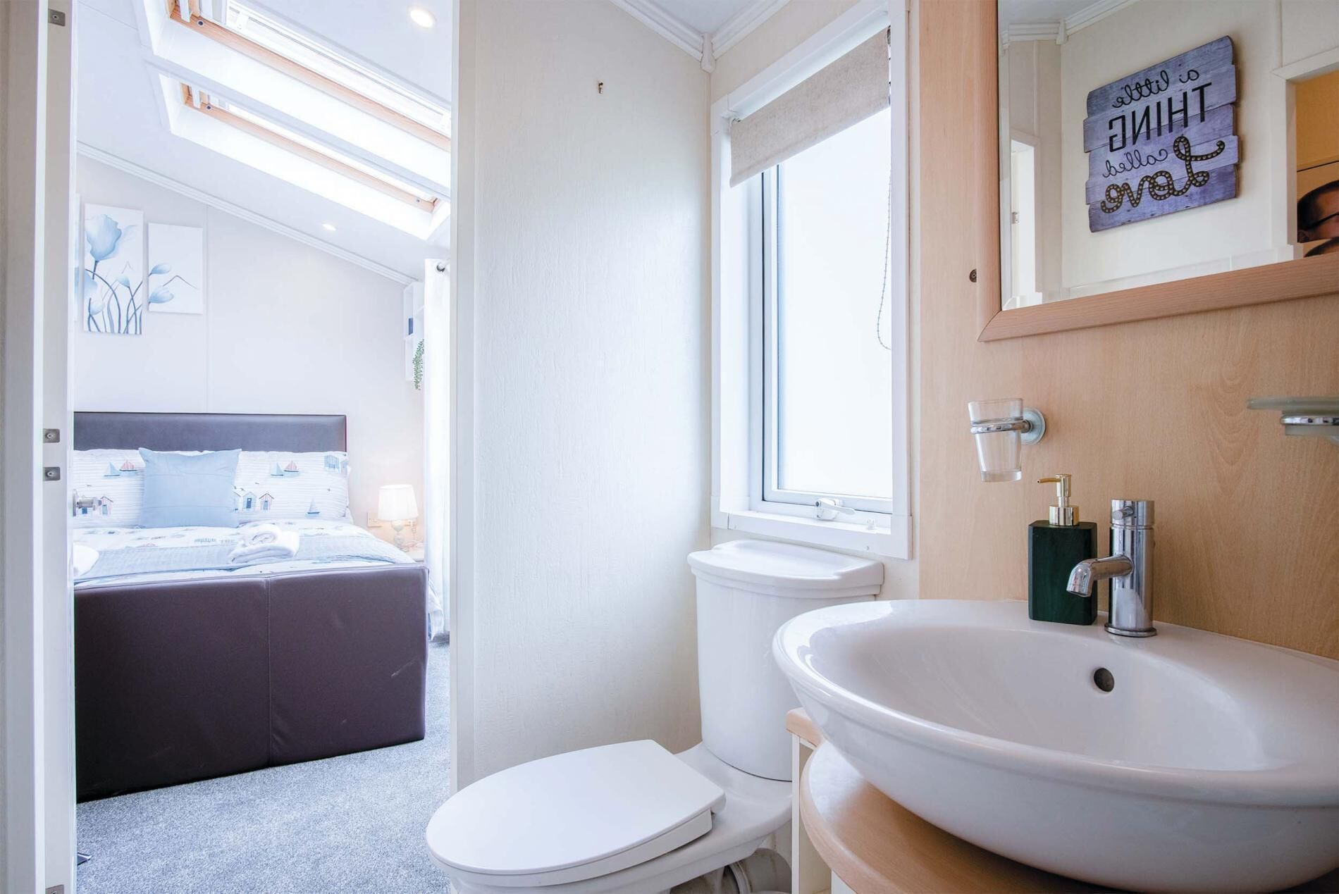 A modern bathroom with a white sink, a toilet, and a shower. There is a window with a towel hanging on the door.