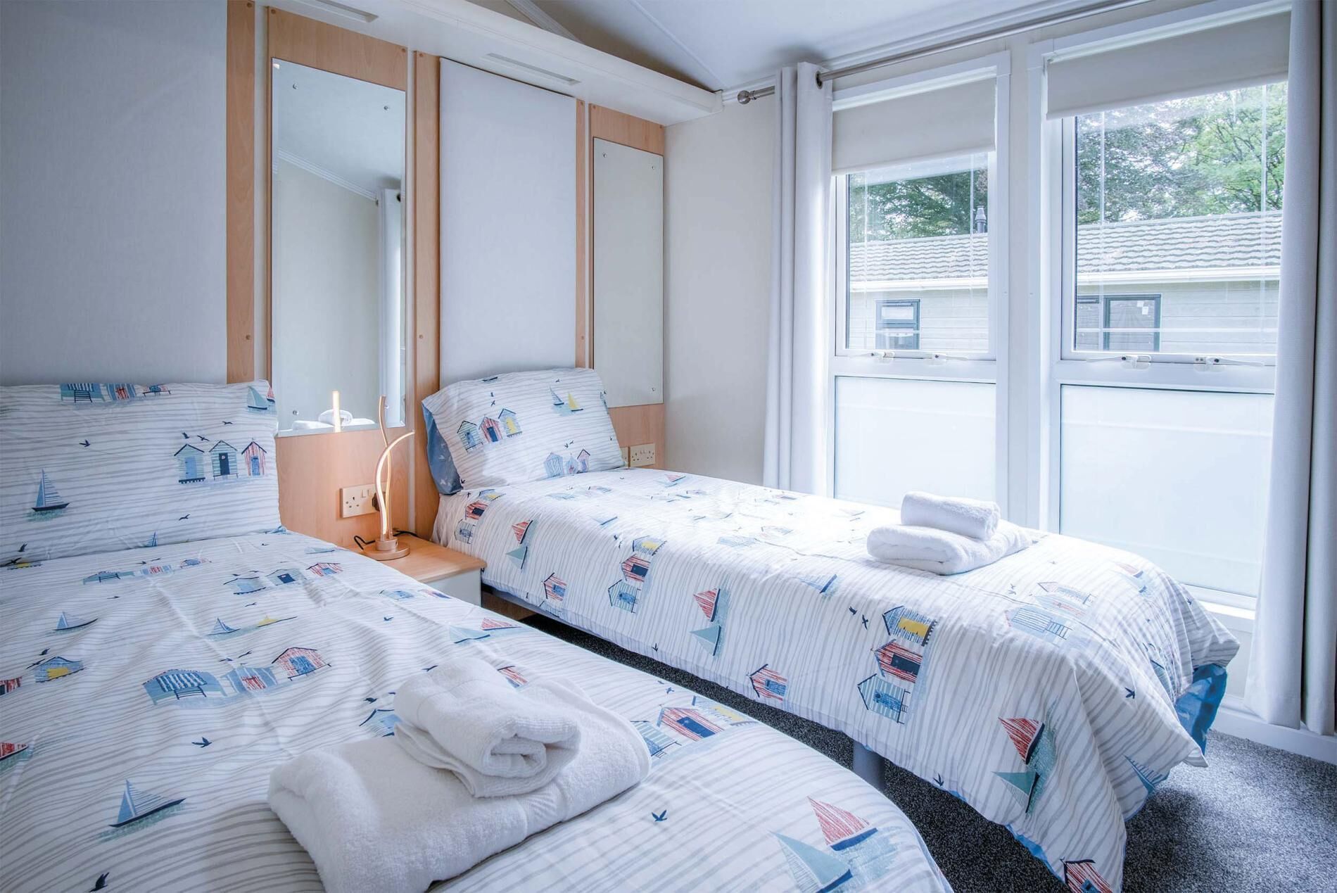 A hotel room with two beds, a large window, and a mirror.