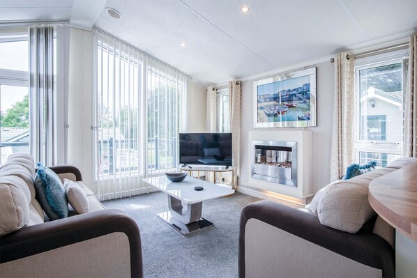 Una sala de estar moderna con una televisión de pantalla plana, una chimenea y ventanas amplias que dan al exterior.