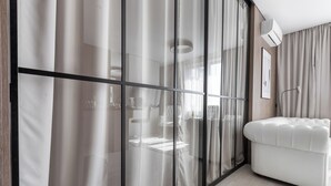 Une pièce moderne avec une cloison en verre, un canapé en cuir blanc et un luminaire fixé au plafond.